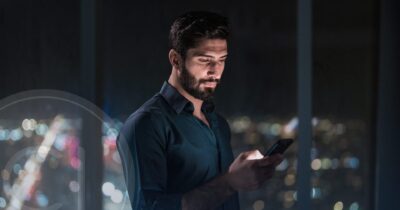 UAE investor checking real estate opportunities on smartphone at night with city lights in background