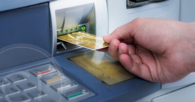 Hand inserting gold credit card into ATM – symbolizing financial freedom and offshore banking through second citizenship