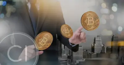 A businessman in a suit reaching out toward three physical-style gold Bitcoin tokens hovering in mid-air, set against a blurred city skyline background.